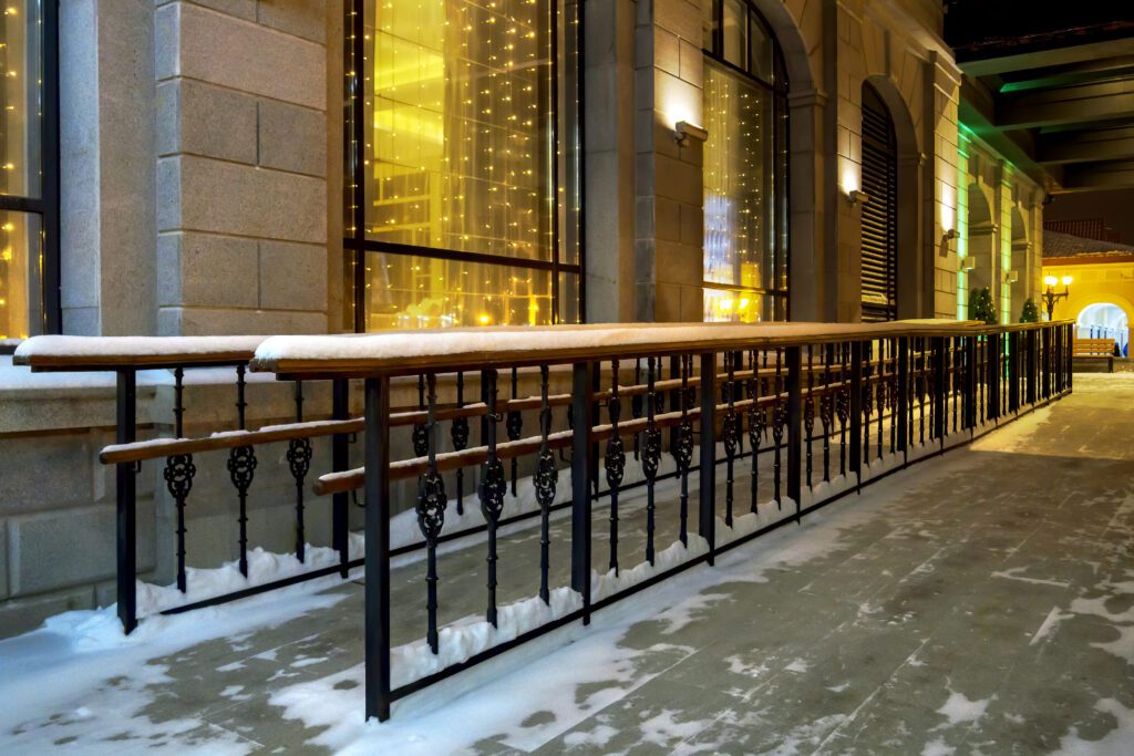 Concrete ramp with wooden handrails that runs along the side of building to the entrance. The setting is a wintry night.