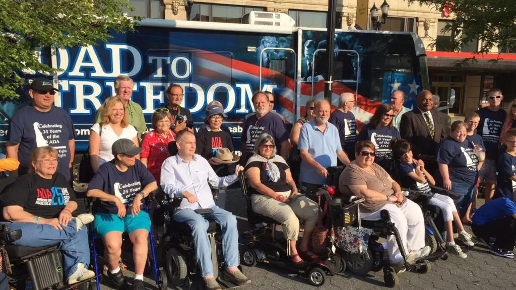 Several people with different types of disabilities in front of the Road to Freedom tour bus.