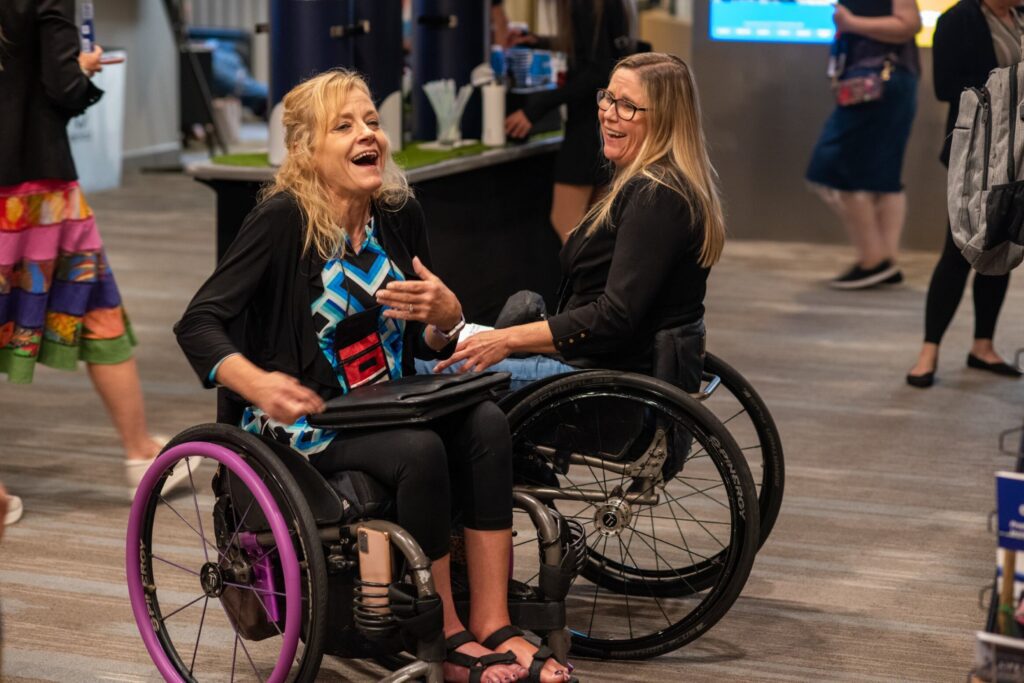 Two women wheelchair users talking and laughing at the National ADA Symposium.